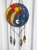 Round stained glass dreamcatcher with blue and yellow Yin Yang symbol is hanging in front of a white aluminum fence panel.jpg