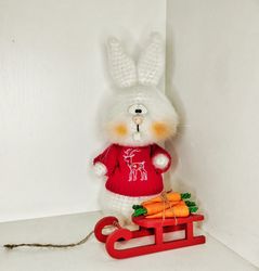 White hare in a jacket with a sleigh and crocheted carrots