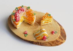 Dolls house miniature food, naked cake with oranges and berries with two cut-off pieces on wooden stand at 1:12 scale