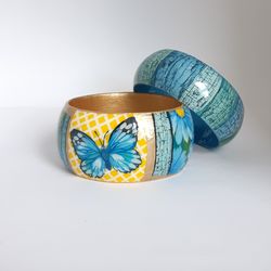 A set of two wide turquoise bracelets . blue-green with a painted butterfly and a floral pattern. Wooden bangles