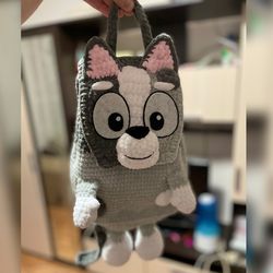 Handmade crochet backpack muffin in shape of a bluey grey dog, perfect for adults and kids. A unique and adorable gift.