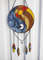 Stained glass dreamcatcher with blue and yellow Yin Yang symbol is hanging in front of a white aluminum fence panel.jpg