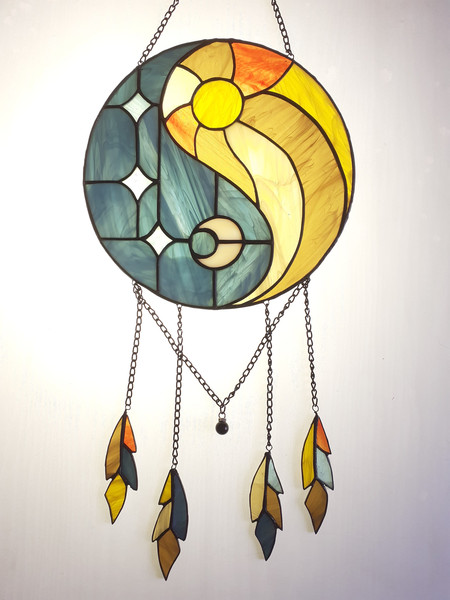 Stained glass dreamcatcher with blue and yellow Yin Yang symbol with hanging chains is lying on a white background.jpg