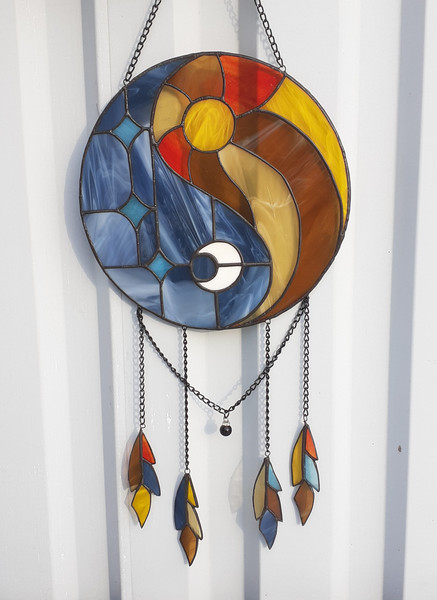 Stained glass dreamcatcher with blue and yellow Yin Yang symbol is hanging in front of a white aluminum fence panel.jpg