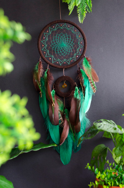 A handcrafted dream catcher with a large brown hoop featuring a vibrant green web and accented with beads. It is adorned with an array of green and brown feathe