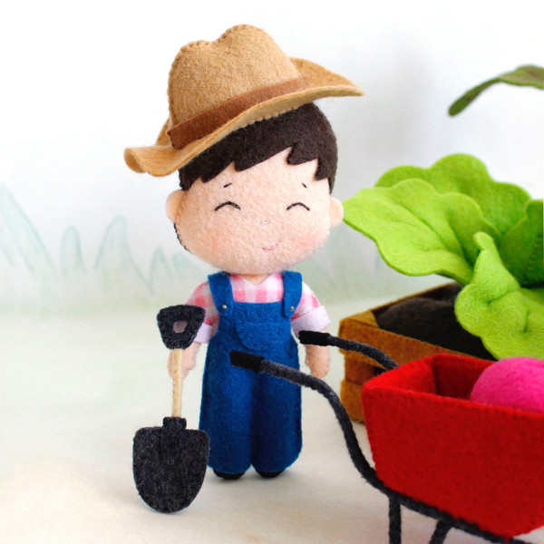 Felt farmer baby boy with a shovel and wheelbarrow near the vegetable garden toys