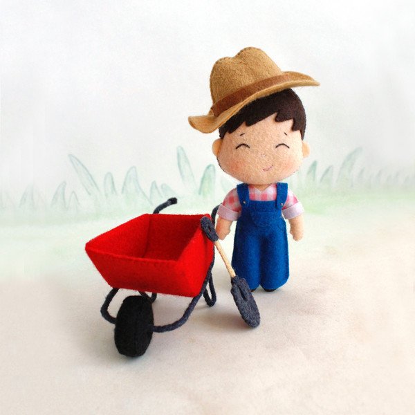 Felt farmer baby boy  in the hat with a shovel and wheelbarrow