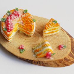 Dolls house miniature food, naked cake with oranges and berries with two cut-off pieces on wooden stand at 1:12 scale