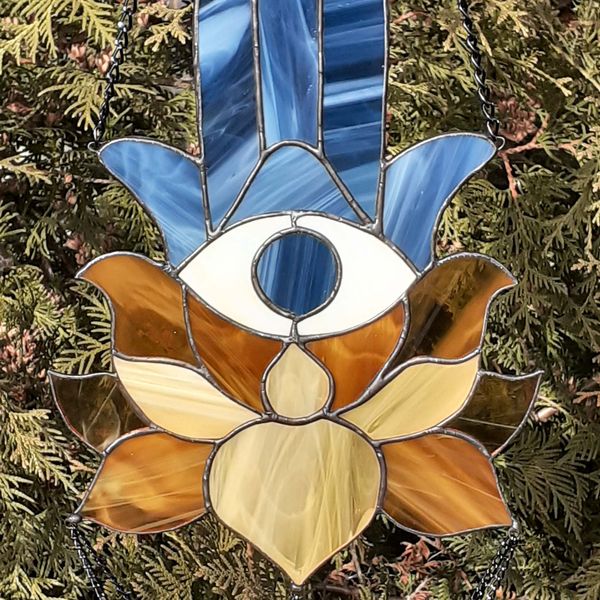 20201108-Blue Stained glass Hamsa suncatcher with brown and beige lotus flower hanging in front of a green Thuja tree.jpg
