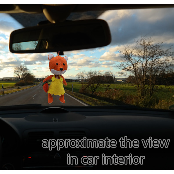 A stitched red fox hangs on a string on the rearview mirror in a car.jpg