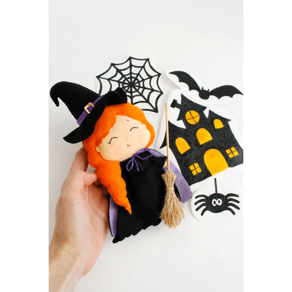 Felt Halloween toy - witch in the pointed hat with a broomstick in the author's hand in the background of painted Halloween decorations
