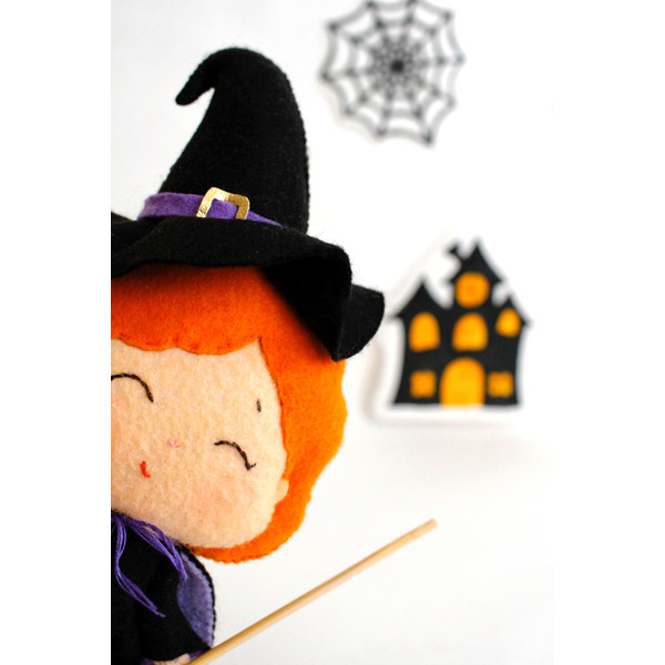 Felt Halloween toy - witch in the pointed hat with a broomstick peeking around the corner in the background of painted Halloween decorations