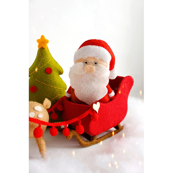 Felt Santa Claus in the Santa's sleigh near the Christmas tree and reindeer Rudolph toys