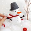Felt snowman toy with a pail on the head on the background of snow and painted trees
