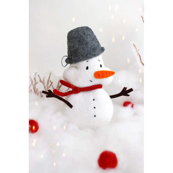 Felt toy snowman with a pail on the head on the background of snow and painted trees