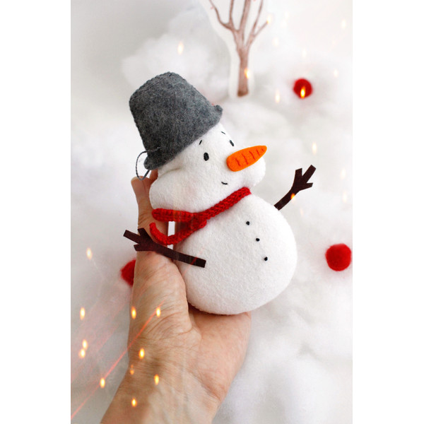 Felt snowman toy with a pail in the author's hand on the head on the background of snow