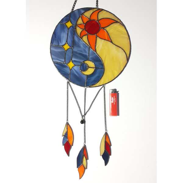 Stained glass Yin Yang dreamcatcher in blue and beige with orange sun and moon next to a red lighter on a white background.jpg