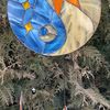 Stained glass Yin Yang dreamcatcher in blue and yellow colors with sun and moon is hanging in front of a Thuja tree.jpg