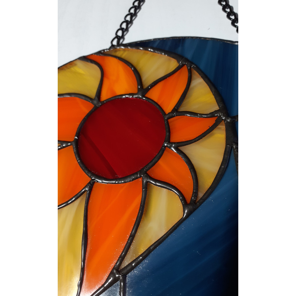 Stained glass depicting orange sun with beige elements with blue glass on the right and solder covered in black patina.jpg