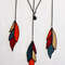 Stained glass feather ornaments in beige, blue, orange and red with black hanging chains on a white background.jpg