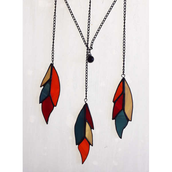 Stained glass feather ornaments in beige, blue, orange and red with black hanging chains on a white background.jpg