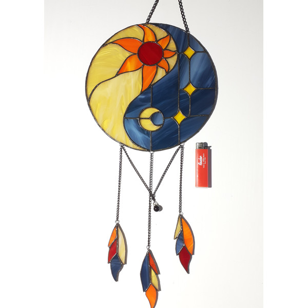 Stained glass Yin Yang dreamcatcher in blue and yellow colors with sun and moon next to a red lighter on a white background.jpg