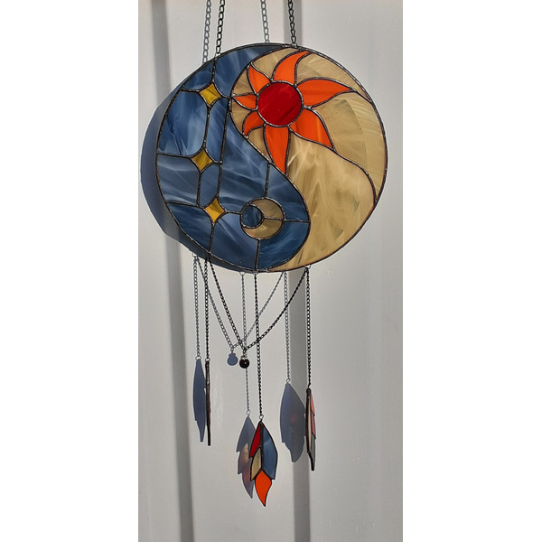 Stained glass Yin Yang suncatcher in art deco style with orange sun and yellow moon symbols in front of a white metal fence.jpg