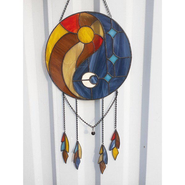 Round stained glass dreamcatcher with blue and yellow Yin Yang symbol is hanging in front of a white aluminum fence panel.jpg