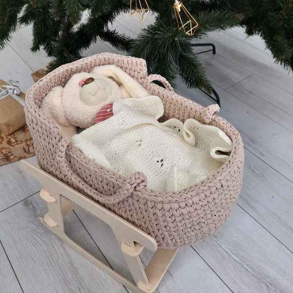 Baby doll basket of beige color handmade on a wooden stand, in which lies a toy doll bunny