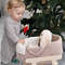 A one-year-old girl rocks a baby doll basket in beige with a milky-white hand-knitted blanket on a wooden stand