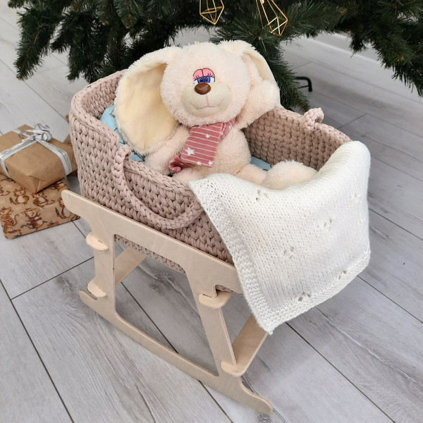 Basket for baby dolls beige handmade on a wooden stand, with a cute bright mattress and milk-white blanket in which sits a toy bunny