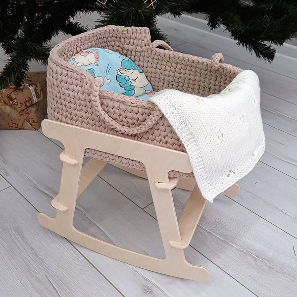 Baby basket for dolls in beige color with milky-white handmade knitted blanket on a wooden stand