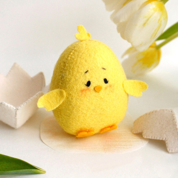 Yellow felt Easter chick near the eggshell and tulips