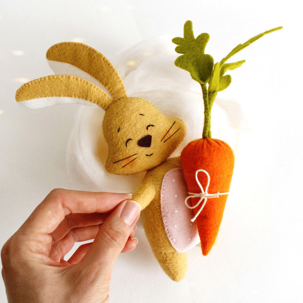 Felt Easter sand color bunny with long ears and bright orange carrot in his hand. Toys in the author's hand.jpg