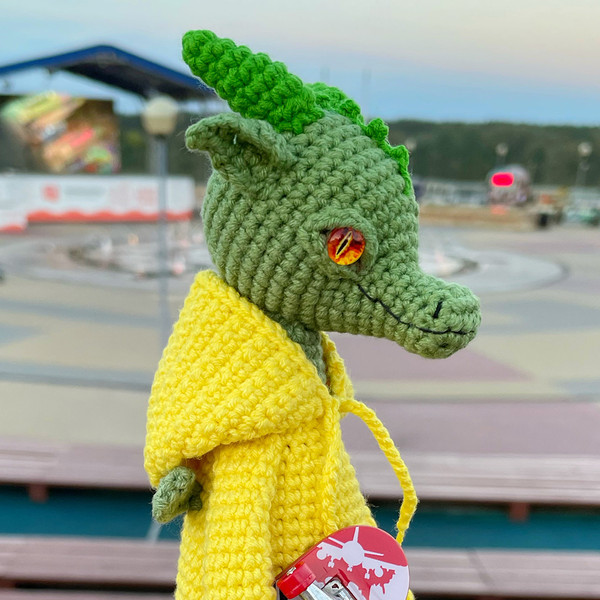 A green knitted stuffed dragon in a yellow hoodie