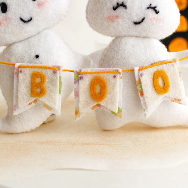Felt ghost boy and girl with BOO garland in the hands standing against the background of painted Halloween decorations, close-up garland view