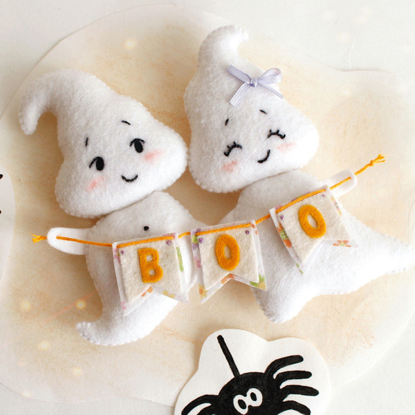 Felt ghost boy and girl with BOO garland laying against the background of painted Halloween decorations, top view