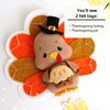 Felt Thanksgiving turkey with pie in the wings laying against the background of painted autumn leaves, front view