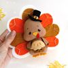 Felt Thanksgiving turkey with pie in the wings laying it the authors hand against the background of painted autumn leaves, top view