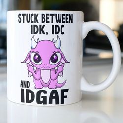 funny snarky dragon coffee mug stating, stuck between idk, idc and idgaf