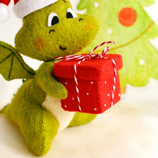 Felt green dragon in Santa cap with red gift box with Christmas presents in his hands