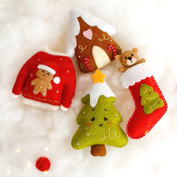 Felt set of toys laying on the snow - smiling Christmas tree, bright red sweater with gingerbread man on it, gingerbread house and red Christmas sock with a lit