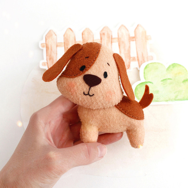 Felt farm animal - cute big dog in the authors hand in the background of painted tree and fence