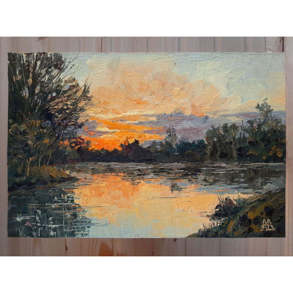 The bright sunset landscape includes a forest on the shore of a calm pond and warm sunlight.