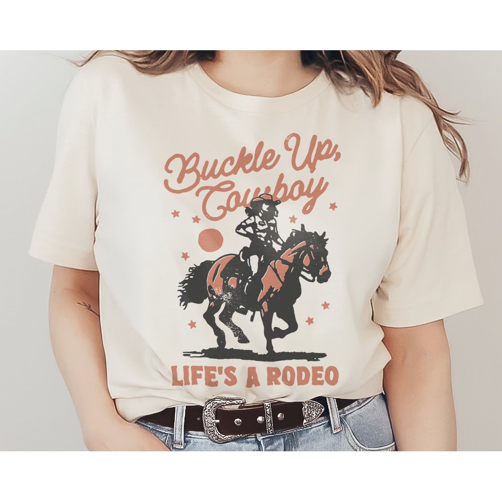 Buckle Up, Cowboy Graphic T-Shirt Life's a Rodeo Country Western Cowgirl Riding Horse Funny Retro Vintage Unisex Men's Women's Tee.jpg